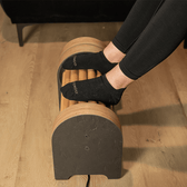 Person using a wooden foot roller for massage therapy on a wooden floor.